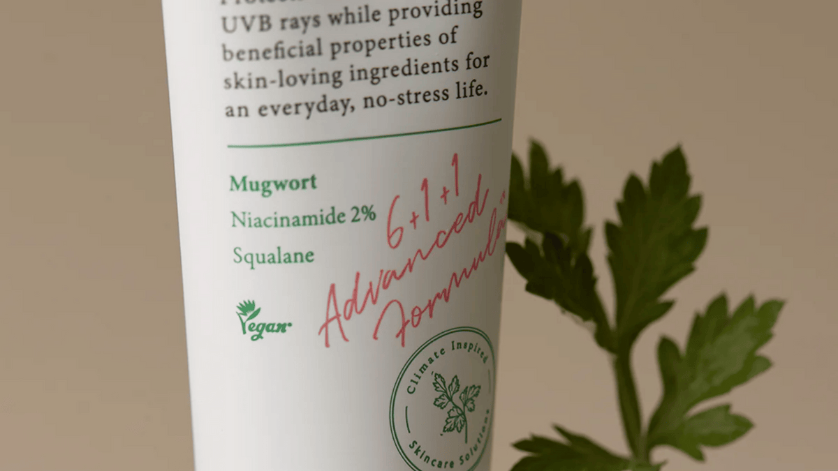 En närbild av en vegansk hudvårdsprodukt med text som lyfter fram ingredienser som mugwort, niacinamid 2 % och squalane. En grön växt visas i bakgrunden, vilket förstärker produktens naturliga och miljövänliga profil.