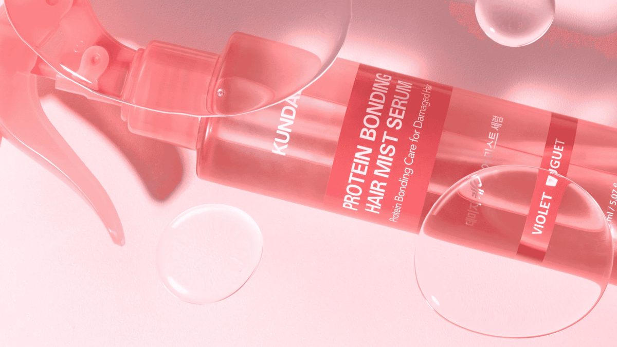 KUNDAL Protein Bonding Hair Mist Serum i rosa sprayflaska med texten Violet Bouquet, liggande mot rosa bakgrund med vattendroppar.
