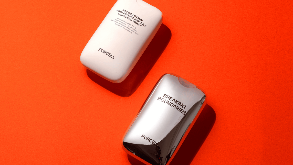 Två flaskor från PURCELL – en vit med texten "24/7 Colostrum Pore Defence Ampoule" och en silvrig med texten "Breaking Boundaries" – ligger på en starkt orange bakgrund.