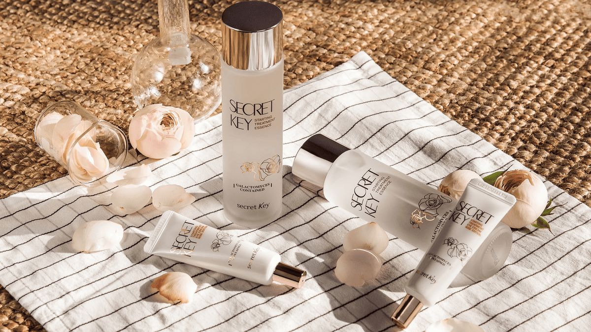 Secret Key Starting Treatment Essence och hudvårdsprodukter placerade på randig duk med rosenblad och glasdetaljer i en estetisk produktuppställning.