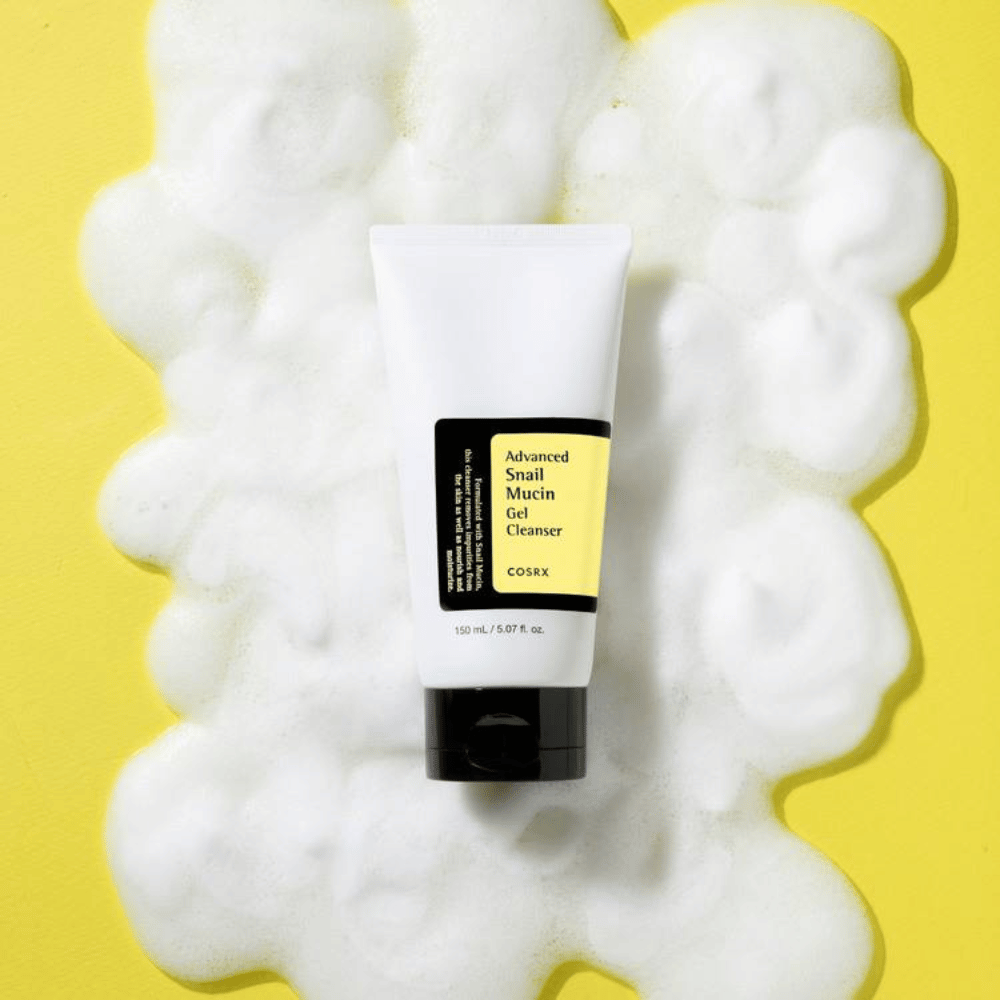 COSRX Advanced Snail Mucin Gel Cleanser 150 ml runsaan vaahdon ympäröimänä keltaisella taustalla – mieto korealainen kasvojen puhdistus snail mucin kosteutukseen ja hehkuun.