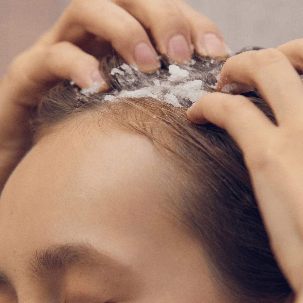 3. AROMATICA Rosemary Scalp Scrub – henkilö hieroo suolakiteitä sisältävää kuorivaa kuorintaa päänahkaan